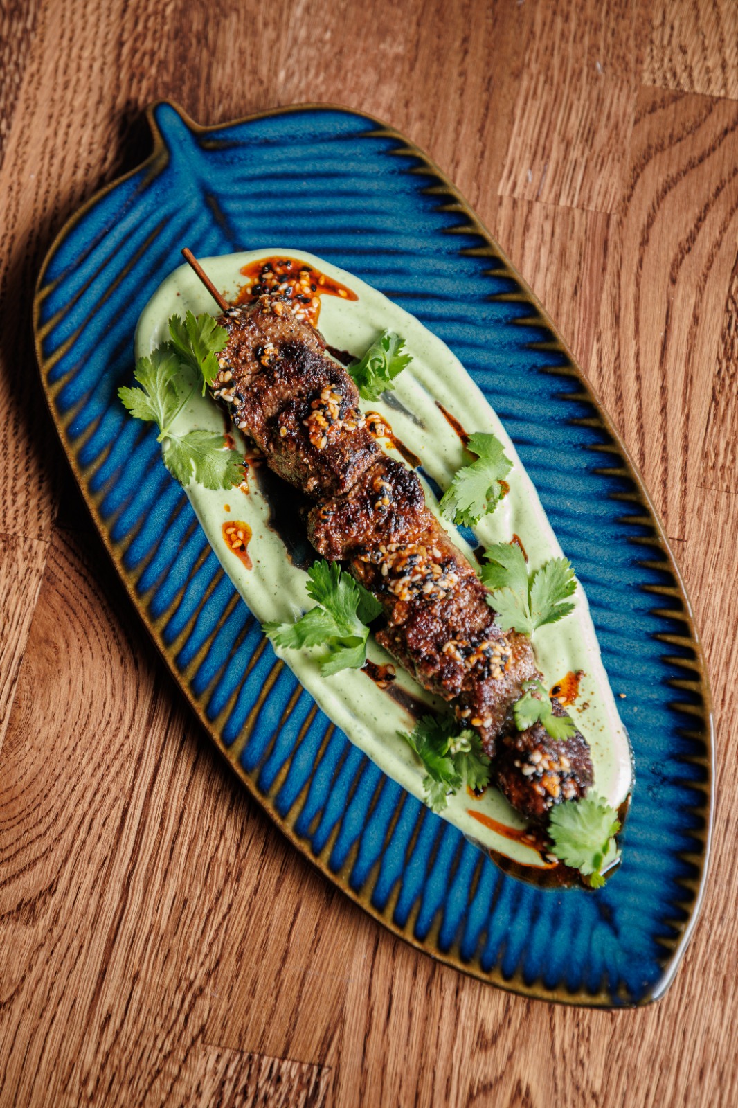 Uyghur Sirloin Kawap on a banana-leaf-shaped plate over garlic yogurt